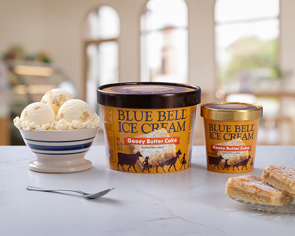 Blue Bell Gooey Butter Cake Ice Cream in half gallon and pint with a bowl sitting on a bakery counter